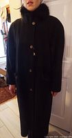 Front view of black wool coat worn on model showing buttons and fur collar