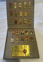 Complete pin set displayed in case, showing all 35 pins arranged in rows with gold Coca-Cola label.