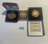 Three gold-colored sports medallions in separate display cases alongside original packaging and certificates.