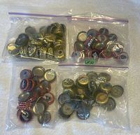 Four clear plastic bags each filled with various NFL beer caps, showcasing multiple team logos and colors clearly visible.