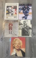 Five pictures arranged on a floor, including hockey cards of Wayne Gretzky, Sidney Crosby, Joe Turner with signature, black and white photo of Elvis Presley, and color photo of Marilyn Monroe.