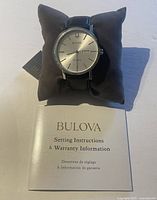 Watch displayed on grey cushion alongside Setting Instructions & Warranty Information booklet.