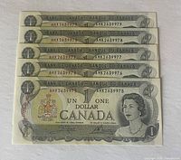 Five sequential 1973 Canadian one dollar bills stacked showing front of notes and visible serial numbers