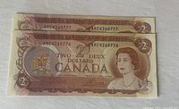 Two Canadian $2 bills from 1974 lying on a flat surface, showing sequential serial numbers AHE4260777 and AHE4260776.