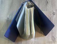 Top view of a large blue three-ring binder filled with empty clear plastic sleeves