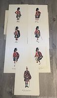 Seven individual colored regimental prints arranged flat on floor showing various Canadian Scottish regiments with soldier portraits in traditional Scottish regalia.