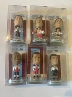 Photo showing six hockey player bobbleheads in clear original plastic packaging, arranged in two rows of three.