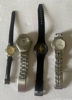 Four wristwatches placed side by side on flat surface showing varied bands and faces.