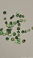 Loose round cut green tsavorite garnet gemstones scattered on a white background.
