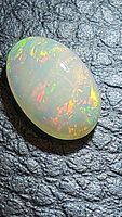 Close-up photo of oval cabochon natural Ethiopian opal showing bright multicolored play of color on textured dark background.