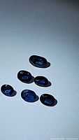 Six oval cut natural royal blue sapphires on a light background showing their deep blue color and facets.