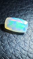 Close-up photo of long cushion cut Ethiopian opal showing multicolored flash of greens, blues, oranges, and chartreuse