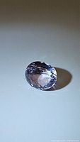 Close-up photo of oval cut pink purple amethyst gemstone on white background with visible facets and coloration.