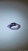 Pear-shaped natural amethyst gemstone placed on a white surface, showing its purple-pink color and faceted pear cut shape.