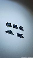 Five natural blue sapphires with mixed cuts and green aquamarine undertones under light, showing clarity and deep blue color.