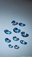 Ten natural Swiss blue topaz gemstones arranged on a light background showing color and facets.