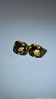 Pair of golden citrine cushion cut gemstones displayed on white background showing the color and clarity of the stones.