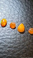 Four natural fire opal gemstones on a textured black surface, showing varying shapes and sizes with orange body color and multicolored flashes.