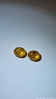 Two natural golden yellow oval cabochon sapphire gemstones placed on white surface with light highlighting inclusions and color.