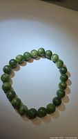 Front view of natural green jade chunky bead bracelet arranged in circle on white background with slight shadowing.