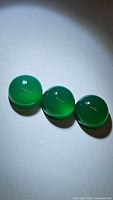 Three round cabochon natural green onyx gemstones, each 10mm, glossy finish, photographed under spotlight showing translucency and smooth surface.