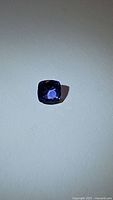 Deep blue cushion cut tanzanite gemstone photographed on a plain surface showing its color and cut.