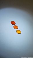 Three oval cabochon mandarin orange carnelian gemstones arranged vertically on white background, showing color gradation from red-orange to yellow-orange.