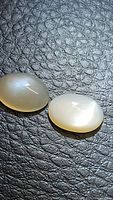 Two natural oval cabochon peach moonstones placed on textured dark surface displaying their smooth surfaces and subtle flash.