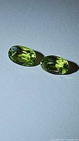 Close-up of the pair of oval cut natural peridot gemstones showing apple green color and clarity on a white background.