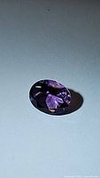 Close-up photo of oval cut purple amethyst gemstone on flat surface showing facets and color.