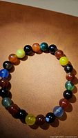Top view of the natural rainbow agate chunky bead stretchy bracelet laid flat on a tan background, showing color variety and bead size.