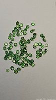 Multiple loose tsavorite garnet gemstones scattered on a white background, highlighting their green color and small round cut shape.