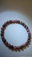 Natural rhodochrosite stretchy bracelet composed of alternating pink and brown patterned beads, displayed circular on neutral background under soft light.