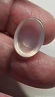 Close-up image of a translucent soft pink oval rose quartz cabochon held between fingers showcasing its smooth polished surface and shape.