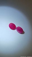 Pair of oval-cut red rubies on white background under normal light