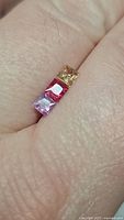 Close-up photo of three natural princess cut sapphires in yellow, red, and purple colors on skin.