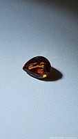 Pear-shaped spessartite garnet gemstone on neutral background, showcasing color and cut.