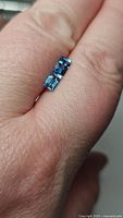 Photo of two baguette cut natural Swiss blue topaz gemstones placed on a finger showing their color and clarity.