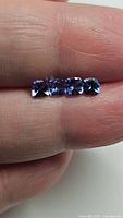 Four deep blue cushion cut tanzanite stones positioned on fingertip for size reference.