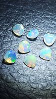 Seven natural untreated faceted Ethiopian opal gemstones in teardrop shapes on a dark textured background.