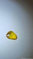Natural golden yellow sapphire gemstone displayed on white background, showing fancy rose cut and transparency under light.