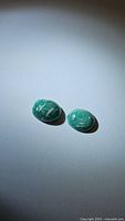 Two natural oval zebra amazonite cabochons placed on white surface, showing color and pattern.