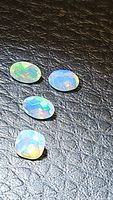 Four small natural Ethiopian opals with faceted oval and cushion cuts, showing rainbow flashes against black background.