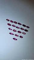 Twenty natural red rubies, marquis and cushion cut, laid out in rows on a white surface under lighting showing color and clarity