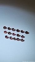 15 individual loose padparadcha sapphires arranged in two rows on a white background, showcasing a pinkish-orange color with diamond facets visible