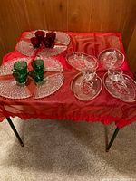 Vintage glass snack plate and cup sets arranged on red cloth table: 8 cut glass fan-shaped plates with 4 ruby red and 4 emerald green cups