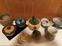 Full assortment of 9 pottery and ceramic items on display table against wood background.