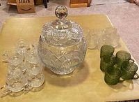 Full set of punch bowl with lid, matching lead crystal cups, assorted green and clear glass cups arranged on a table.