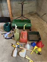 Front view of the gardening and outdoor tools lot with Scotts spreader, watering cans, funnels, spray bottles, and containers visible
