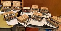 Overview of nine wooden boxes each containing groups of painted cavalry figures on a table
